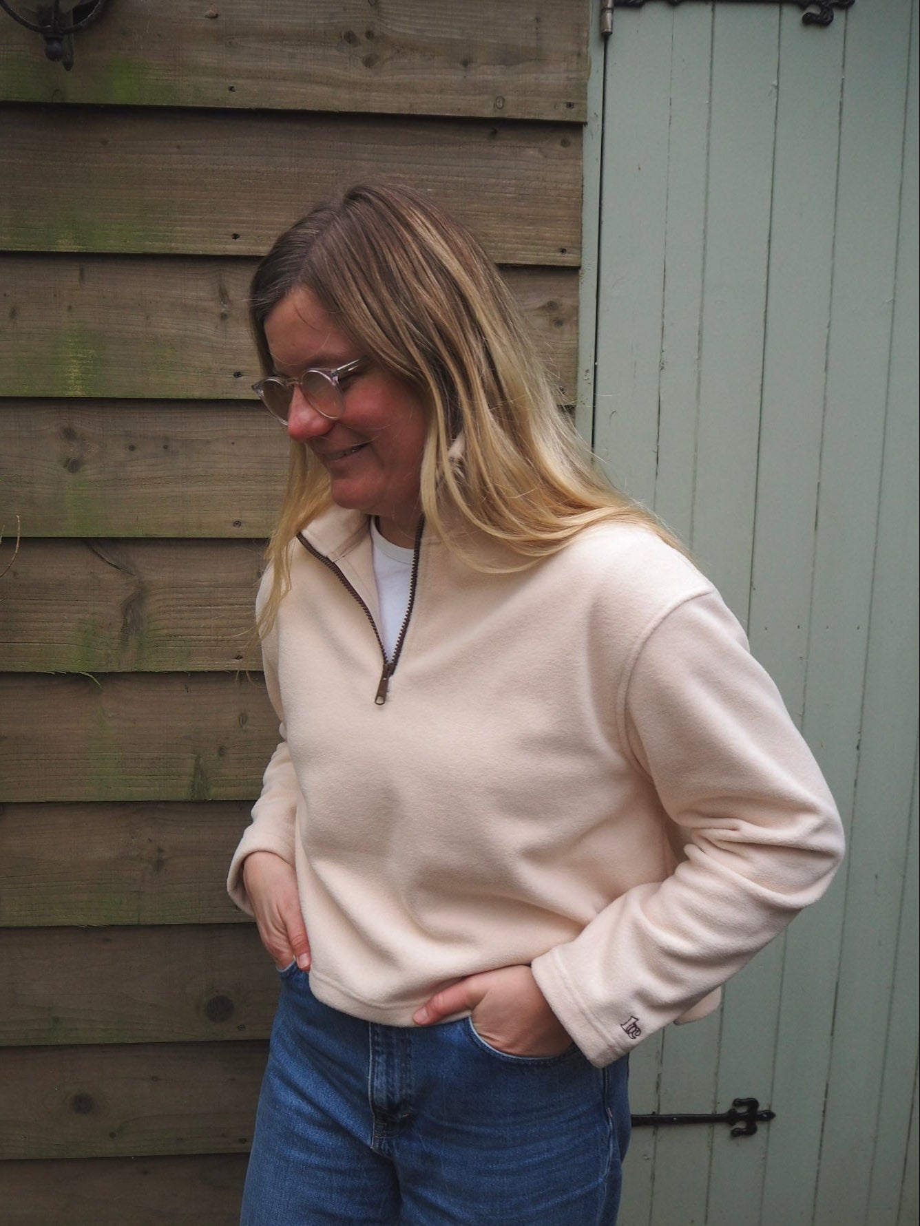 Charlotte is wearing the Courchevel cream fleece 1/4 zip with a white t-shirt underneath, standing in the countryside. 