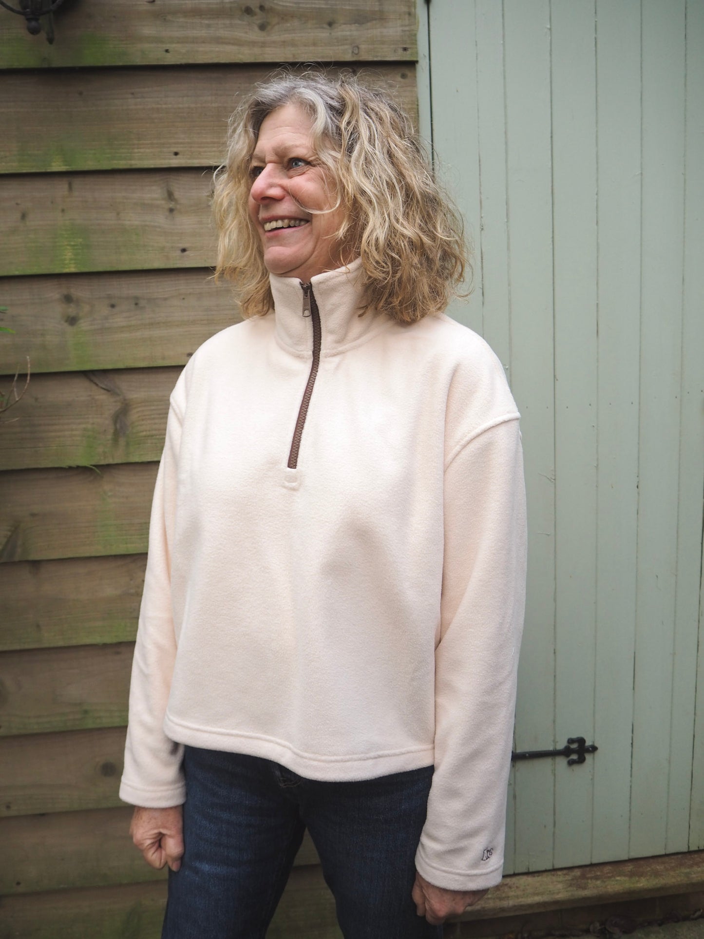 Sallie is wearing the Courchevel cream fleece 1/4 zip with a white t-shirt underneath, standing in the countryside. 