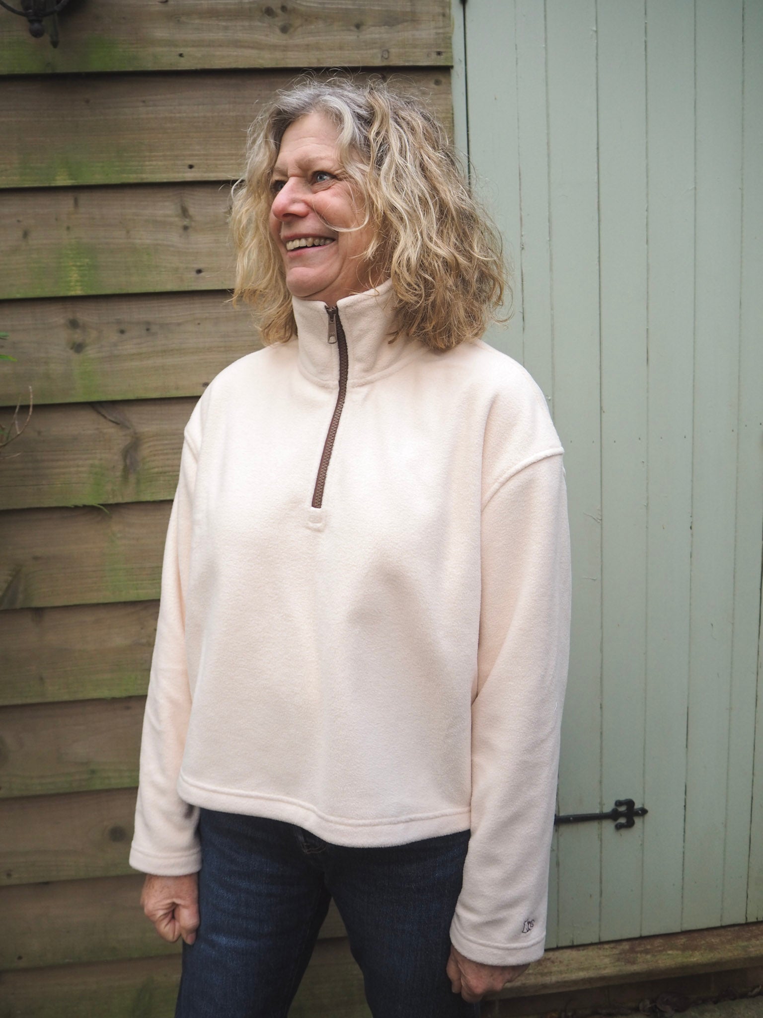 Sallie is wearing the Courchevel cream fleece 1/4 zip with a white t-shirt underneath, standing in the countryside. 