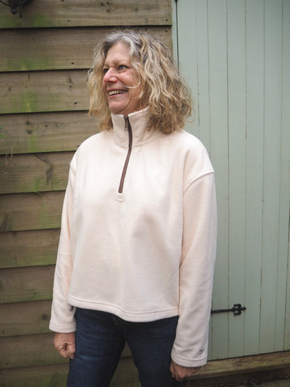 Sallie is wearing the Courchevel cream fleece 1/4 zip with a white t-shirt underneath, standing in the countryside. 