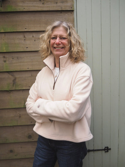Sallie is wearing the Courchevel cream fleece 1/4 zip with a white t-shirt underneath, standing in the countryside. 