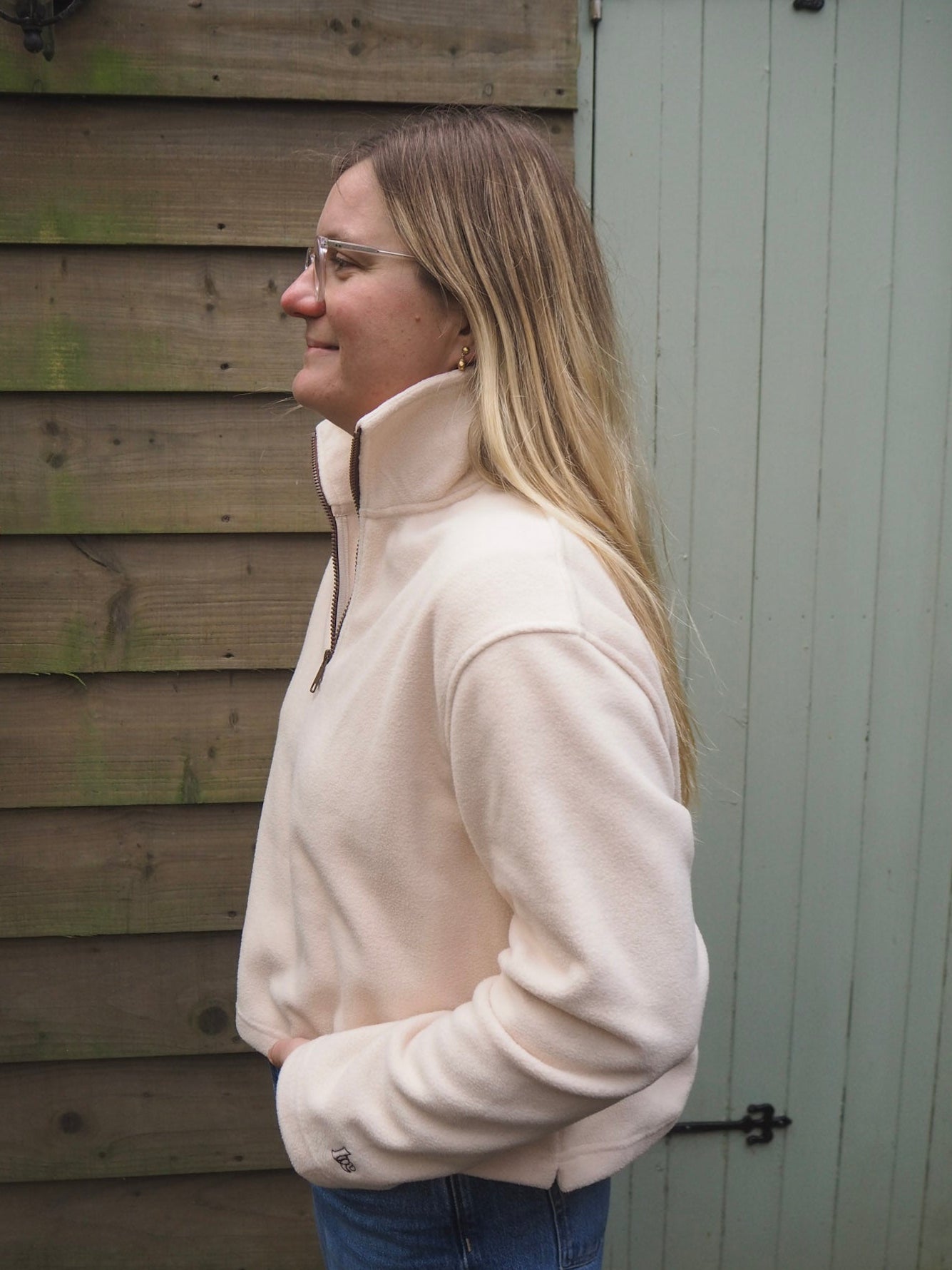 Charlotte is wearing the Courchevel cream fleece 1/4 zip with a white t-shirt underneath, standing in the countryside. 