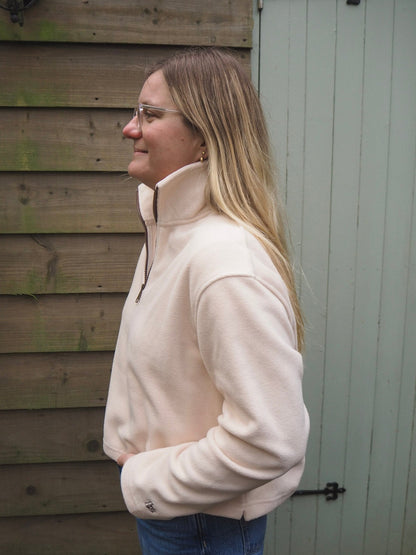Charlotte is wearing the Courchevel cream fleece 1/4 zip with a white t-shirt underneath, standing in the countryside. 