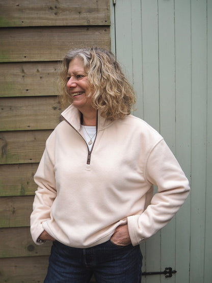 Sallie is wearing the Courchevel cream fleece 1/4 zip with a white t-shirt underneath, standing in the countryside. 