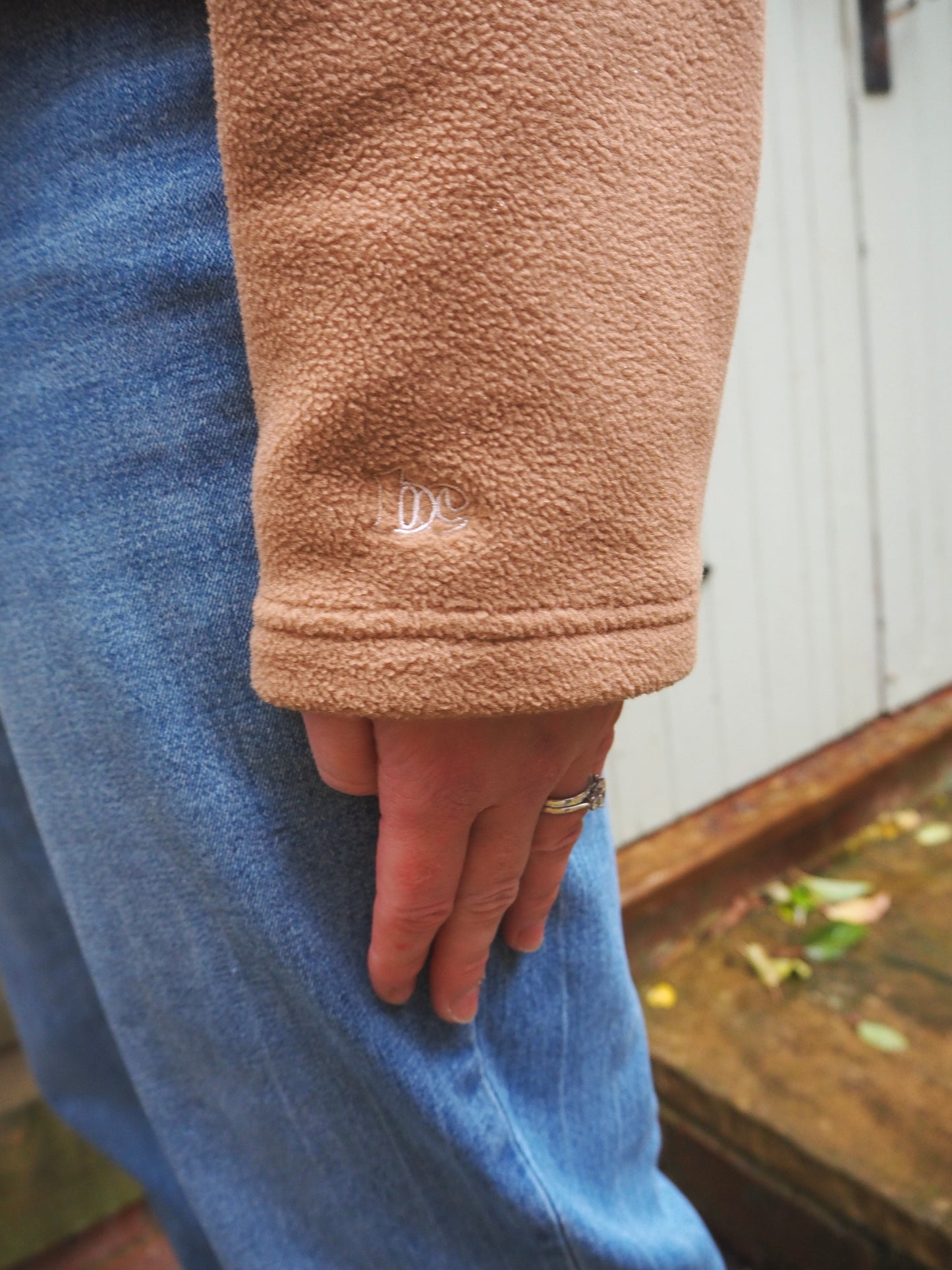 Close-up of Maddi wearing the Jaipur camel fleece 1/4 zip with blue jeans in the countryside. 