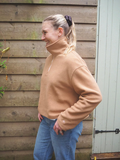 Our model Maddi wearing The Jaipur camel fleece pullover with jeans, standing outside in the countryside. 