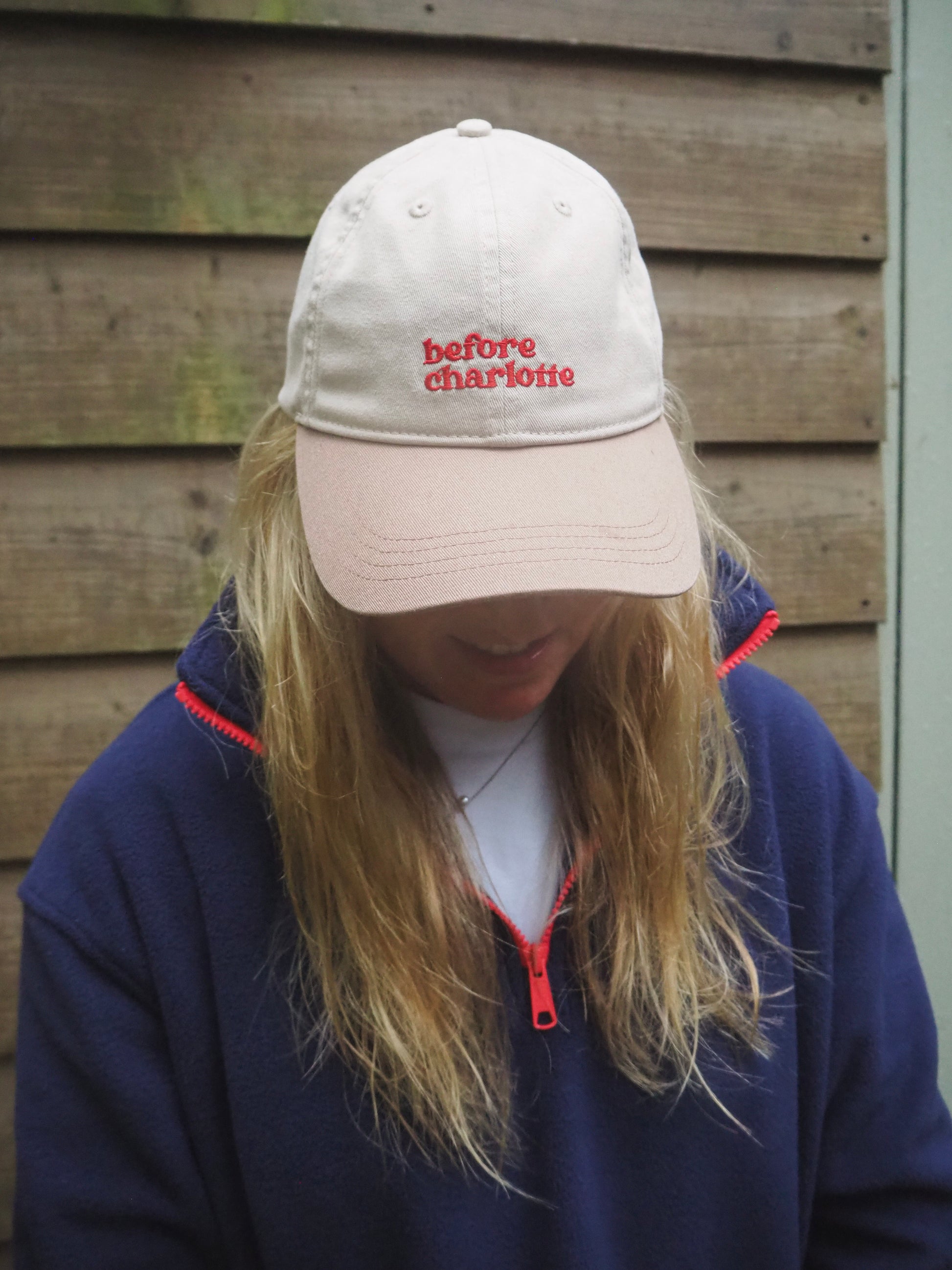 Maddi wearing a two-tone beige cap with 'before charlotte' text against a wooden background