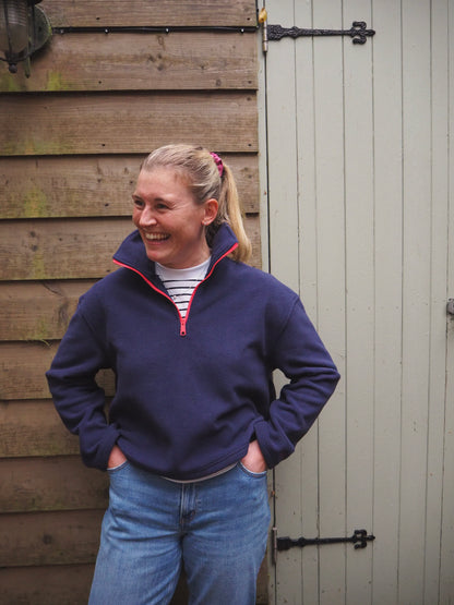 Maddi is wearing the Nantucket navy blue fleece 1/4 zip with a striped t-shirt underneath, standing in the countryside. 