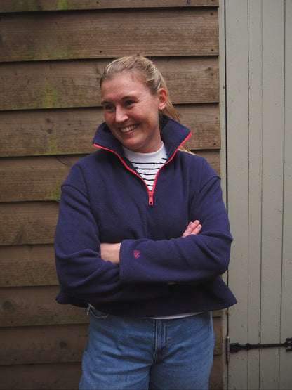 Maddi is wearing the Nantucket navy blue fleece 1/4 zip pullover with a striped t-shirt underneath, standing in the countryside. 